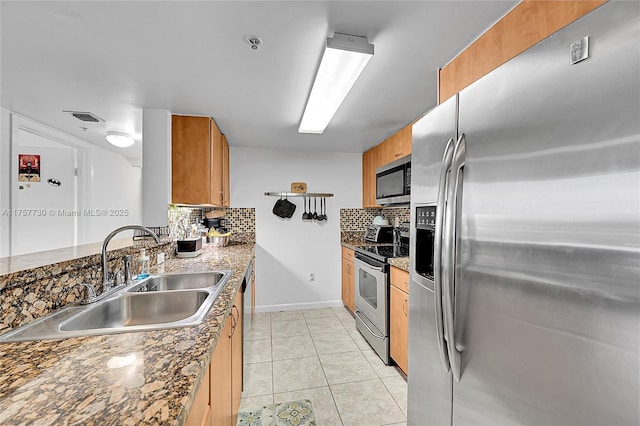 kitchen with light tile patterned floors, tasteful backsplash, appliances with stainless steel finishes, brown cabinetry, and a sink