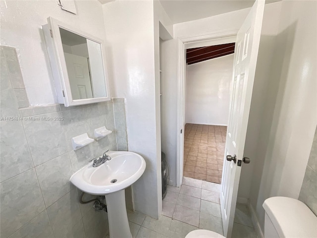 bathroom with a sink, tile patterned flooring, toilet, and tile walls