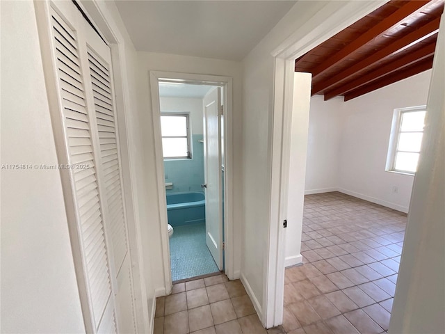 hall with vaulted ceiling with beams, baseboards, and light tile patterned flooring