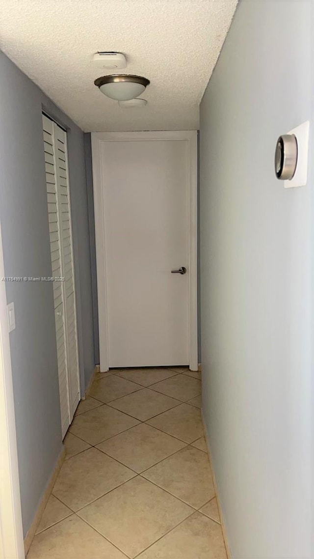 corridor featuring light tile patterned flooring, a textured ceiling, and baseboards