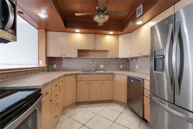 kitchen with light brown cabinets, a tray ceiling, appliances with stainless steel finishes, and a sink