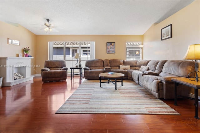 living area with ceiling fan, a textured ceiling, vaulted ceiling, and wood finished floors