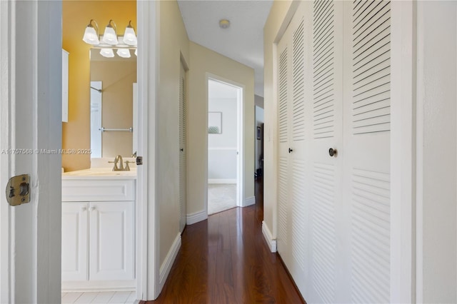 hallway with dark wood-style flooring, a sink, and baseboards