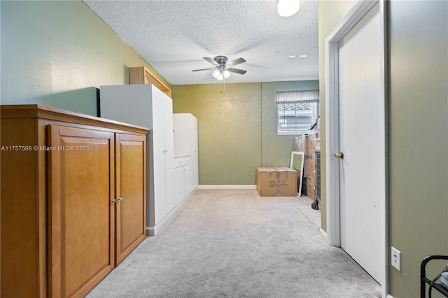 hall with light carpet, baseboards, and a textured ceiling