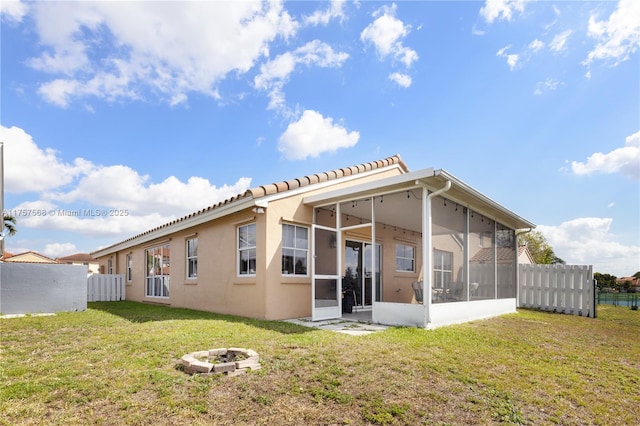 back of property featuring a fire pit, fence, a sunroom, a lawn, and stucco siding