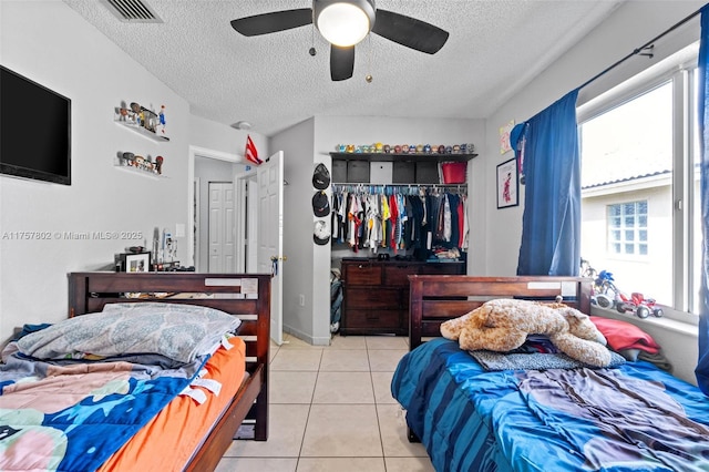 tiled bedroom with a textured ceiling, a closet, visible vents, and a ceiling fan