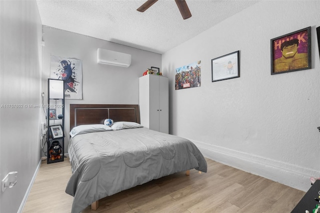 bedroom with light wood-type flooring, a wall mounted air conditioner, a textured ceiling, and baseboards