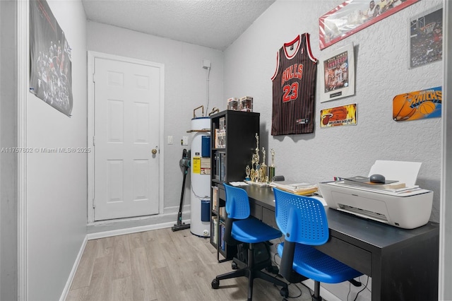 office space featuring light wood finished floors, a textured wall, electric water heater, a textured ceiling, and baseboards