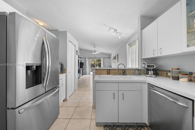 kitchen featuring light tile patterned flooring, stainless steel appliances, a peninsula, a sink, and white cabinets