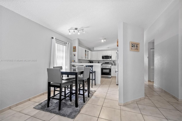 dining space featuring lofted ceiling, light tile patterned flooring, a textured ceiling, and baseboards