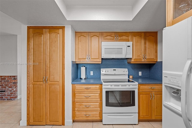 kitchen featuring light tile patterned floors, brown cabinets, white appliances, and dark countertops