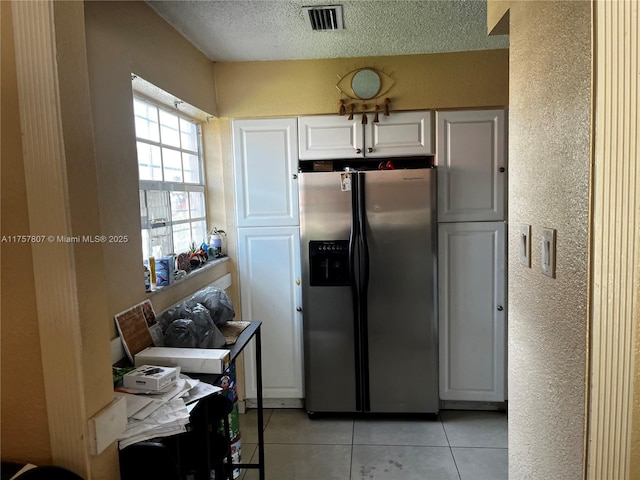 kitchen with stainless steel fridge, visible vents, white cabinets, a textured wall, and light tile patterned flooring