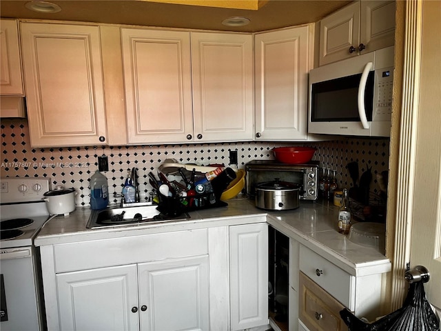 kitchen with white appliances, range hood, light countertops, white cabinetry, and a sink