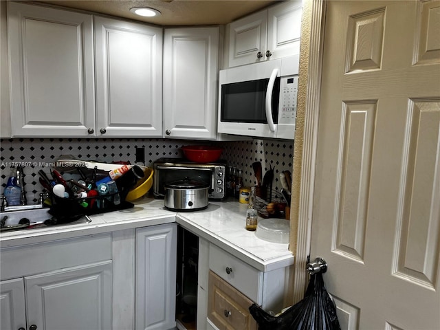 kitchen with light countertops, white microwave, white cabinetry, and decorative backsplash