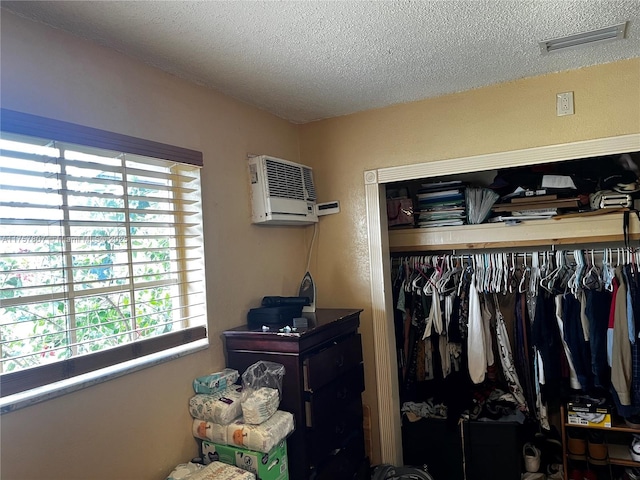 bedroom featuring a wall unit AC, multiple windows, visible vents, and a textured ceiling