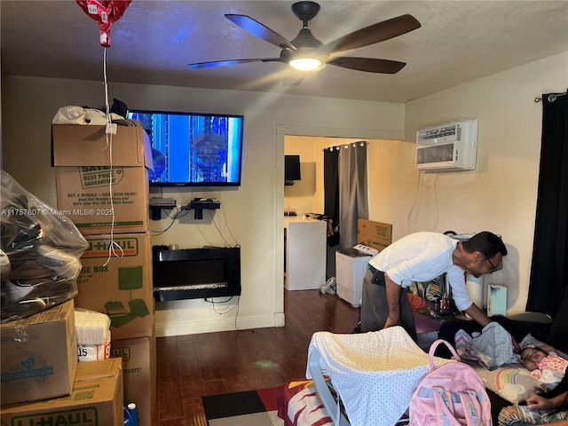 living area featuring baseboards, a ceiling fan, an AC wall unit, and wood finished floors