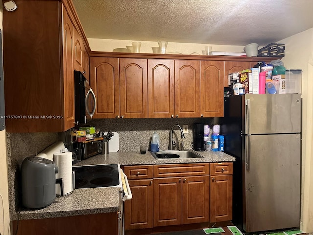 kitchen with a textured ceiling, stainless steel appliances, brown cabinetry, and a sink