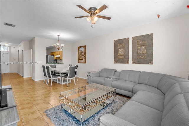 living area featuring ceiling fan with notable chandelier, light tile patterned flooring, visible vents, and baseboards