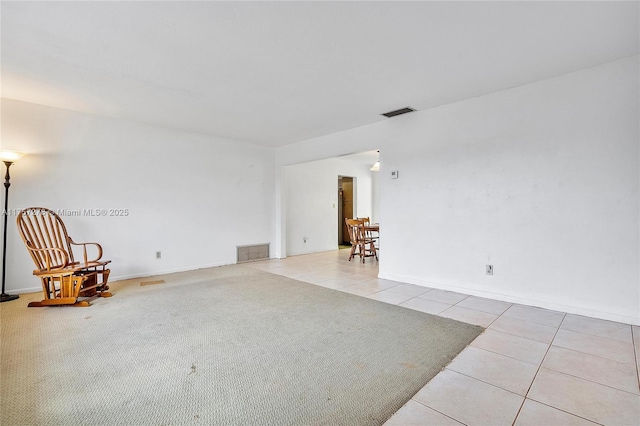 empty room featuring light tile patterned floors, baseboards, visible vents, and light colored carpet