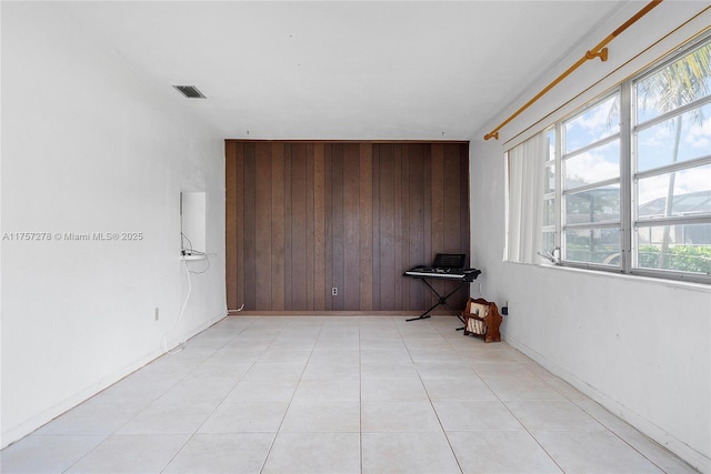 spare room featuring visible vents, wooden walls, baseboards, and light tile patterned flooring