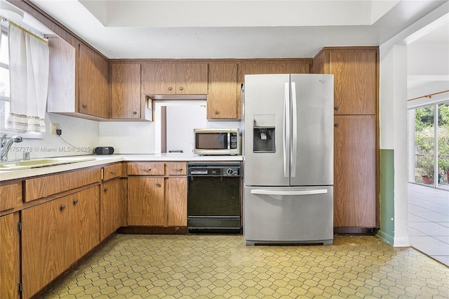 kitchen with brown cabinets, stainless steel appliances, a sink, and light countertops