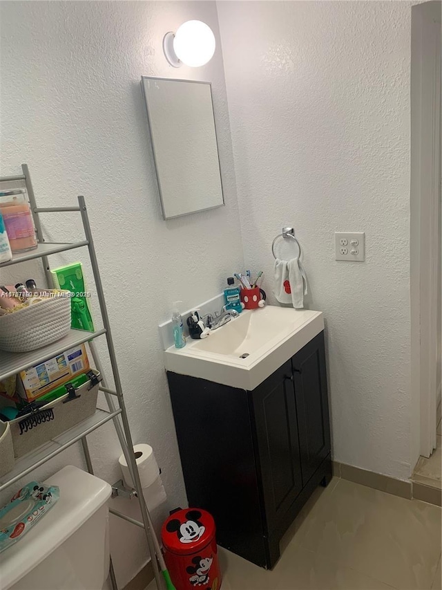 half bathroom with a textured wall, vanity, and toilet