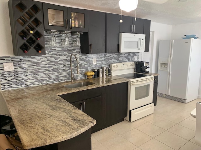 kitchen with white appliances, decorative backsplash, glass insert cabinets, dark cabinets, and a sink