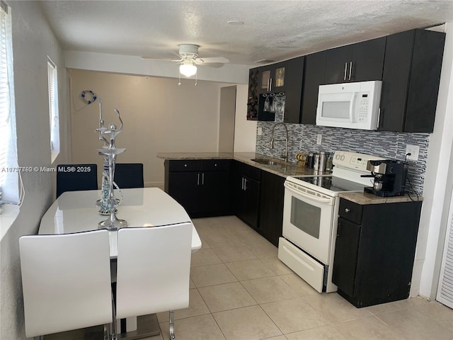 kitchen with dark cabinets, a peninsula, white appliances, a sink, and decorative backsplash