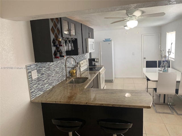 kitchen with light tile patterned floors, a textured ceiling, a peninsula, white appliances, and decorative backsplash