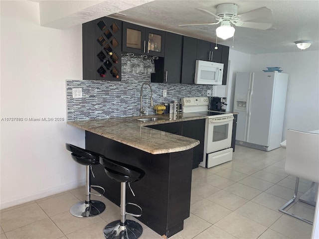 kitchen featuring a breakfast bar, decorative backsplash, white appliances, dark cabinetry, and a peninsula