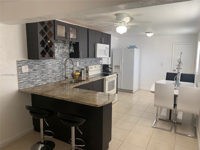 kitchen with light tile patterned floors, a peninsula, white appliances, decorative backsplash, and glass insert cabinets