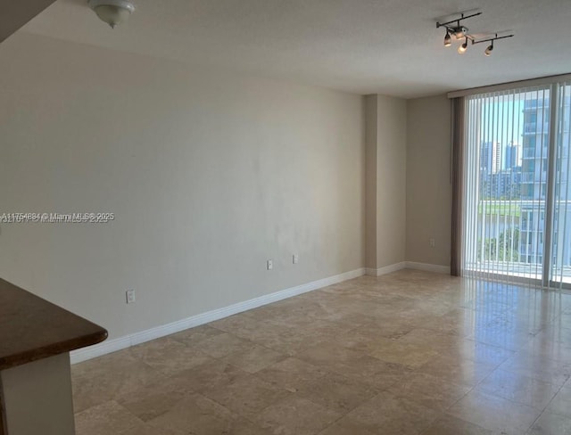 spare room featuring rail lighting, baseboards, and a wall of windows