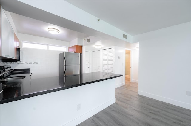 kitchen with stainless steel appliances, dark countertops, visible vents, wood finished floors, and a peninsula