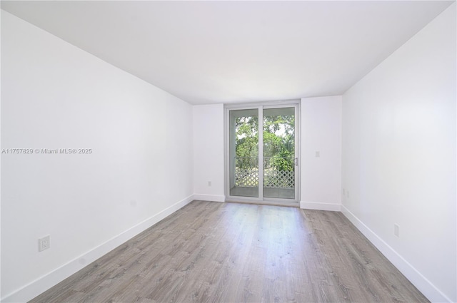 spare room featuring baseboards, a wall of windows, and wood finished floors