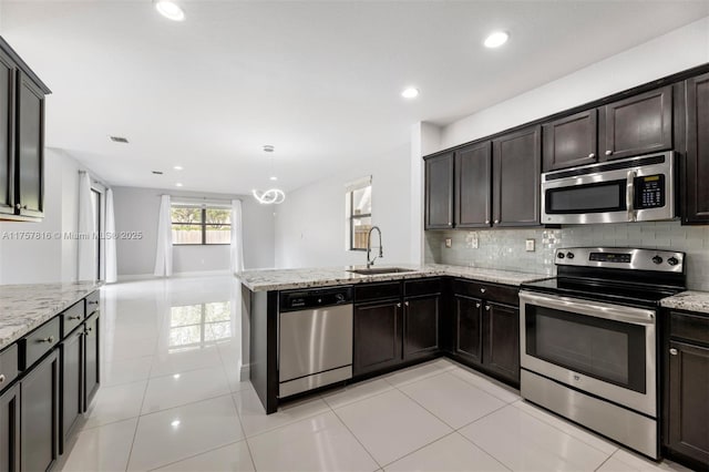 kitchen featuring a peninsula, appliances with stainless steel finishes, decorative backsplash, and a sink