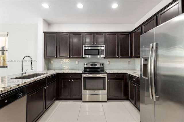 kitchen featuring dark brown cabinetry, a sink, appliances with stainless steel finishes, backsplash, and light stone countertops