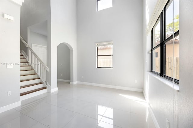 unfurnished room with arched walkways, a high ceiling, baseboards, and a healthy amount of sunlight