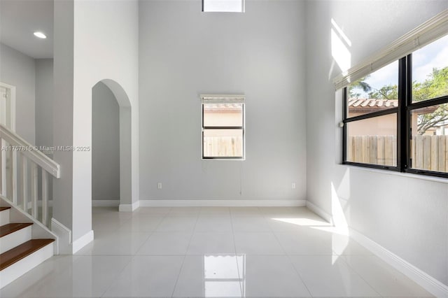 tiled spare room with arched walkways, a high ceiling, stairway, and baseboards