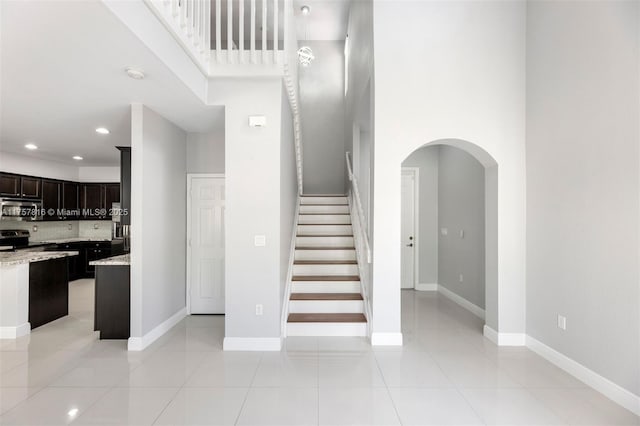 stairway with arched walkways, tile patterned flooring, recessed lighting, a towering ceiling, and baseboards