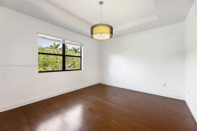 unfurnished room featuring dark wood-type flooring, a tray ceiling, and baseboards