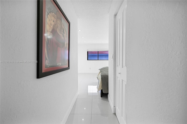 hall with light tile patterned floors, baseboards, a textured ceiling, and a textured wall