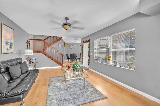 living area with wood-type flooring, stairs, baseboards, and ceiling fan