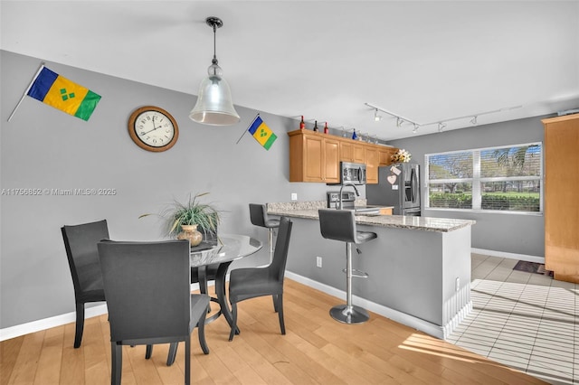 dining room with light wood-type flooring, baseboards, and track lighting