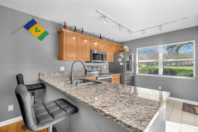 kitchen with light stone counters, stainless steel appliances, a sink, a peninsula, and baseboards