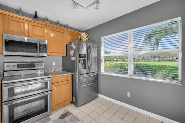 kitchen featuring light tile patterned floors, baseboards, appliances with stainless steel finishes, brown cabinets, and track lighting