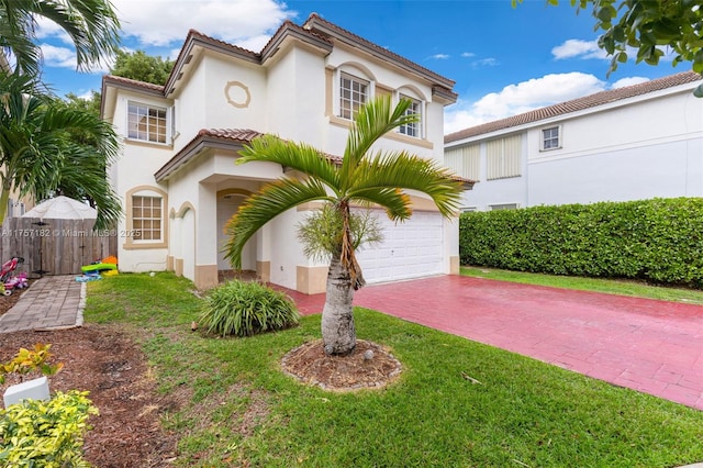 mediterranean / spanish home featuring decorative driveway, a tile roof, stucco siding, a front yard, and fence