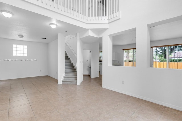 empty room featuring stairs, light tile patterned floors, and baseboards