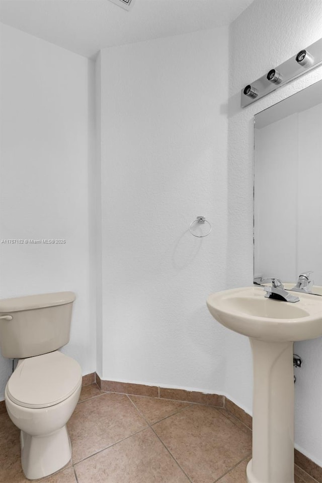 half bathroom with a sink, tile patterned flooring, toilet, and baseboards