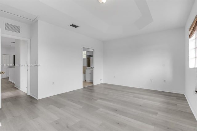 empty room featuring a raised ceiling, visible vents, and light wood-style flooring