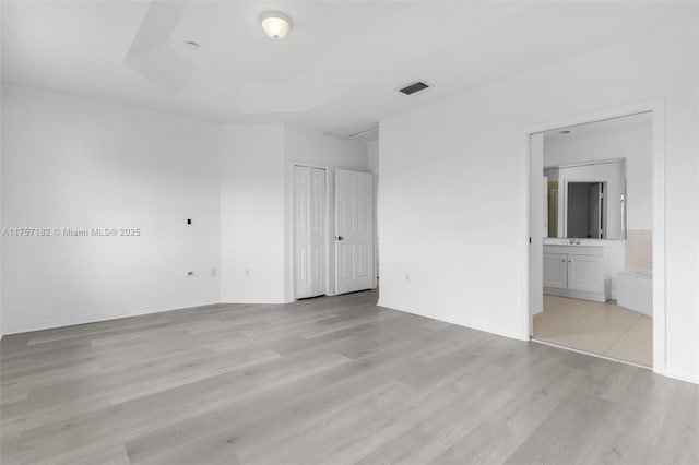 unfurnished bedroom with connected bathroom, visible vents, light wood-style floors, a closet, and a tray ceiling